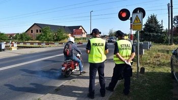 Policjant z sokistą przy zamkniętym szlabanie, kierowca skutera.