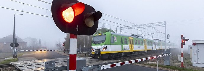 Pociąg na przejeździe, zamknięte rogatki, pulsujące światło