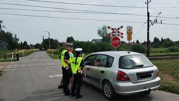 Policjanci podczas akcji ulotkowej stoją obok samochodu przed przejazdem.