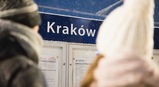 Podróżni stojący przed tablicą z rozkładem jazdy.