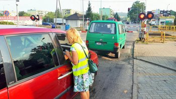 Koordynator wręcza ulotkę kierowcy w samochodzie stojącym przed zamkniętym przejazdem.